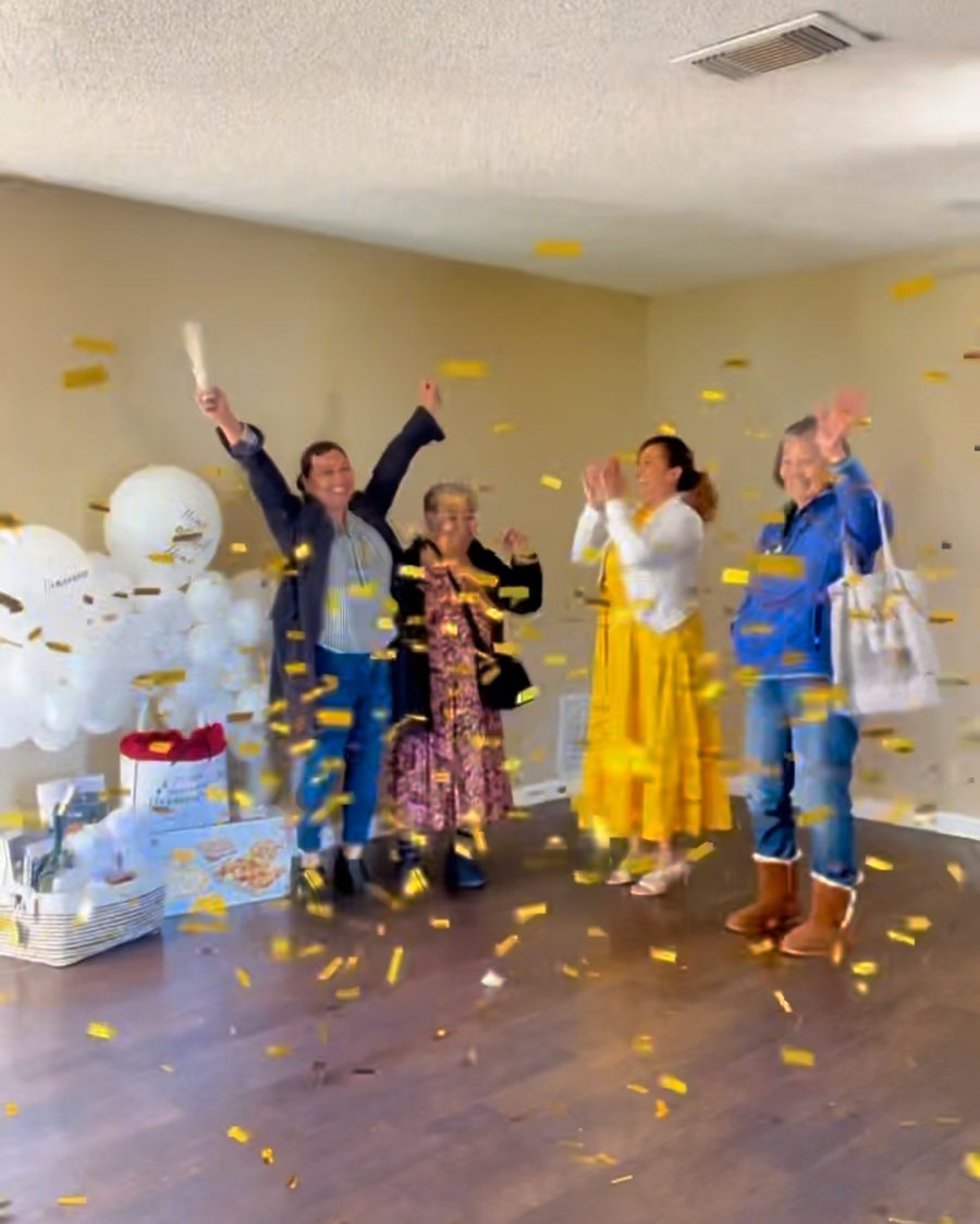 A family celebrating with confetti and balloons in the empty living room of the home they just bought